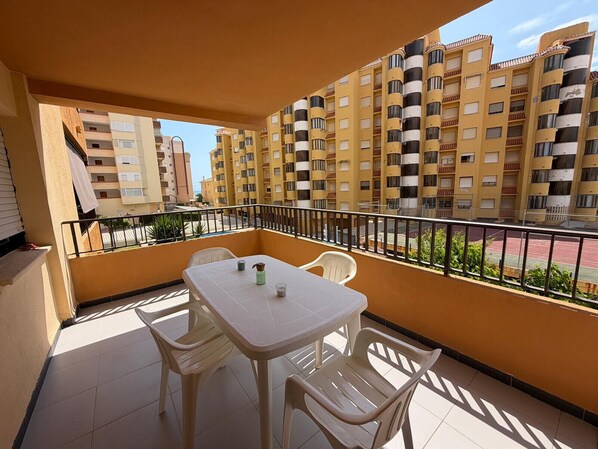 A balcony with a table and chairs, a railing, and a view of multi-story buildings.