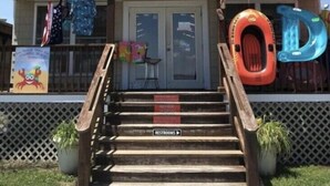 Une boutique de plage avec une enseigne indiquant « BOUTIQUE DE PLAGE » et des marches menant à l’entrée.