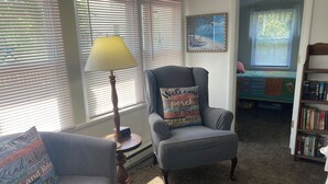 Un salon chaleureux avec un fauteuil gris, une petite table avec une lampe et une bibliothèque.