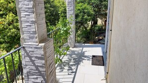 Un escalier orné de piliers en pierre, une rampe en métal et une vue sur la verdure et un bâtiment au loin.