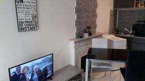 Une cuisine moderne avec un mur d’accent en pierre, un coin repas équipé d’un téléviseur et un petit espace salon.