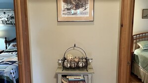 Un pasillo con una pequeña mesa que sostiene libros y una cesta metálica decorativa. Encima de la mesa, un cuadro enmarcado cuelga de la pared.