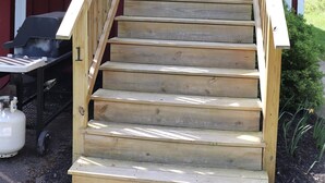 Una escalera de madera que lleva a un edificio rojo con un ventanal blanco y un pequeño porche.