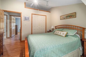 A bedroom with a bed, a nightstand, a lamp, a door, and a hallway leading to another room. - Breezy Acres Farm Apt 1- large yard, fire pit, game room near Cooperstown (Cooperstown)