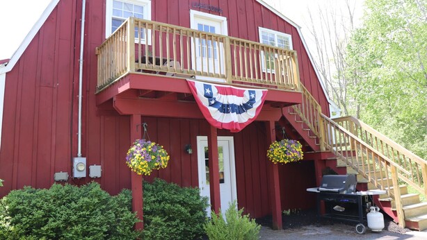 Ein rotes Bauernhaus mit einem hölzernen Balkon, einer Flagge und bepflanzten Blumenkörben.