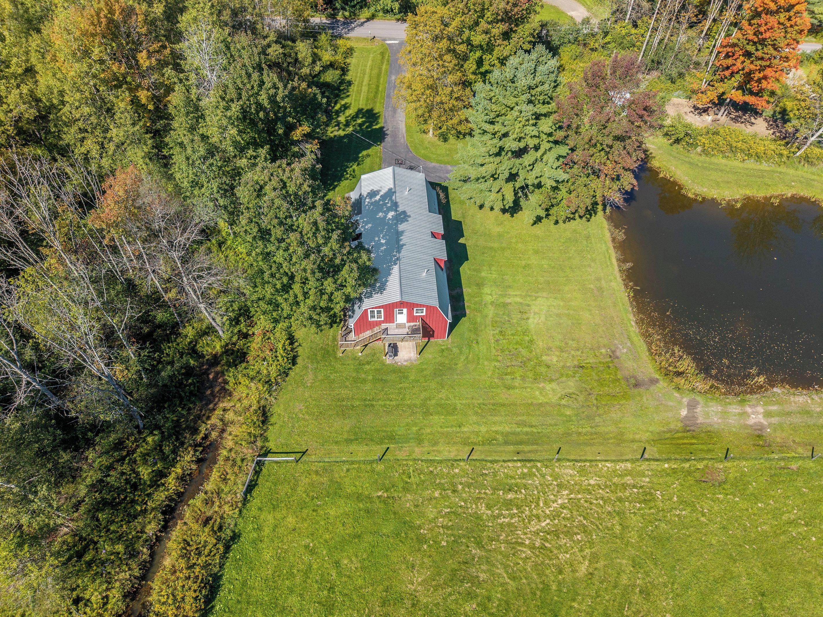 An aerial view of a property with a red barn, a pond, and a well-maintained lawn.