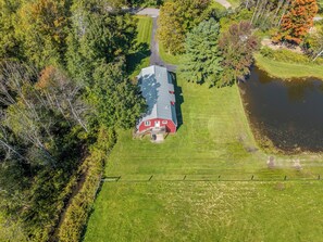An aerial view of a property with a red barn, a pond, and a well-maintained lawn.