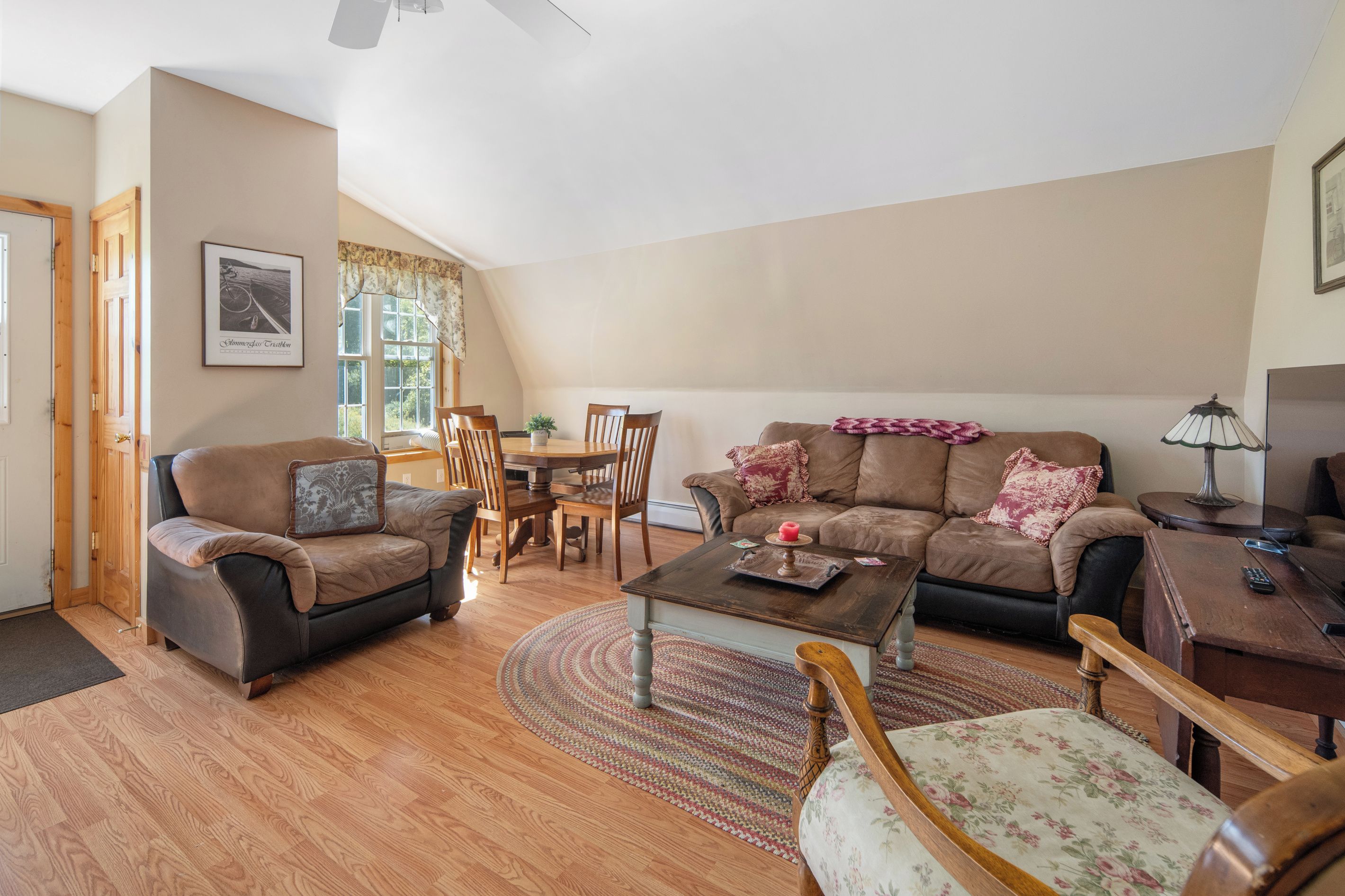 A living room with a brown sofa, a coffee table, a dining table with chairs, and a lamp.
