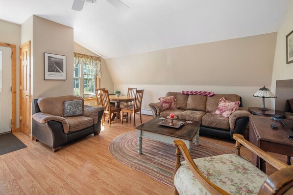 A living room with a brown sofa, a coffee table, a dining table with chairs, and a lamp.