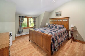 A bedroom with a wooden bed, a window with curtains, a bedside table with a lamp, and a radiator.