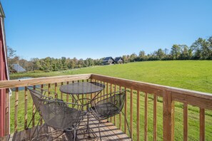 A wooden deck with a table and chairs, overlooking a grassy field and a row of houses.