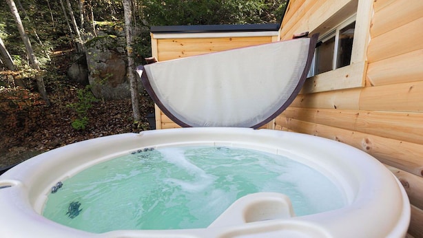A hot tub with a control panel, surrounded by wooden cabin walls and a natural forest backdrop. - Rockhouse Cabin — Front Row View to Rock Formations (Rockbridge)