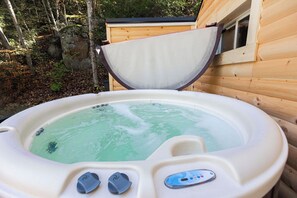 A hot tub with a control panel, surrounded by wooden cabin walls and a natural forest backdrop.