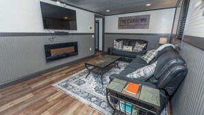A cozy living room with a sofa, a coffee table, and a flat-screen TV mounted on the wall. - Rockhouse Cabin — Front Row View to Rock Formations (Rockbridge)