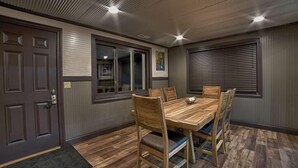 A dining area with a wooden table and chairs, a door, a window, and a ceiling light. - Rockhouse Cabin — Front Row View to Rock Formations (Rockbridge)