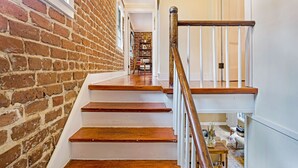 Un escalier avec des marches en bois et des rampes blanches, menant à une pièce dont un mur est en briques et qui possède une porte.