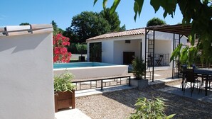 Un espace piscine agrémenté d’une pergola, de sièges extérieurs et d’un bâtiment blanc doté d’un toit en tuiles.