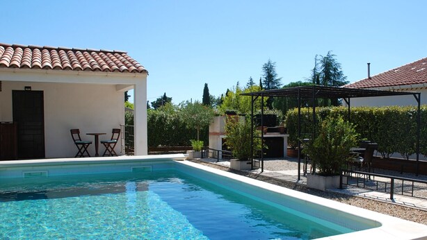 Une piscine avec une terrasse carrelée, une pergola et des sièges d’extérieur.