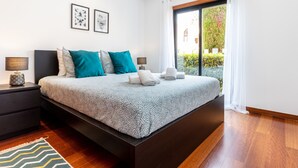 Une chambre moderne avec un grand lit, deux tables de chevet et une vue sur un jardin, visible par la fenêtre.
