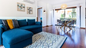 Un salon avec un canapé bleu, un tapis à motifs et un coin repas comprenant des chaises et une table.