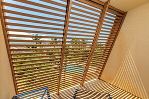 Un balcon avec des lattes en bois, une vue sur des palmiers et un ciel dégagé.