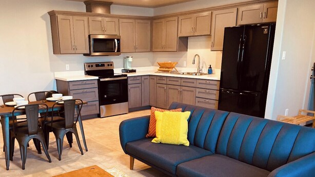 A modern kitchen with a black refrigerator, microwave, and stove. There is a blue sofa with yellow pillows and a wooden coffee table. - "BRAND NEW" 2 bedroom, 1 bath duplex/home  (Yuma)