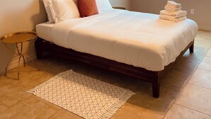 A neatly made bed with white linens and a red pillow, a small round side table, a patterned rug, and a macrame hanging decoration. - "BRAND NEW" 2 bedroom, 1 bath duplex/home  (Yuma)