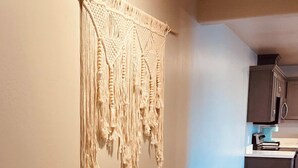A hallway with a macramé wall hanging, a kitchen area with cabinets and a trash can, and a tiled floor. - "BRAND NEW" 2 bedroom, 1 bath duplex/home  (Yuma)