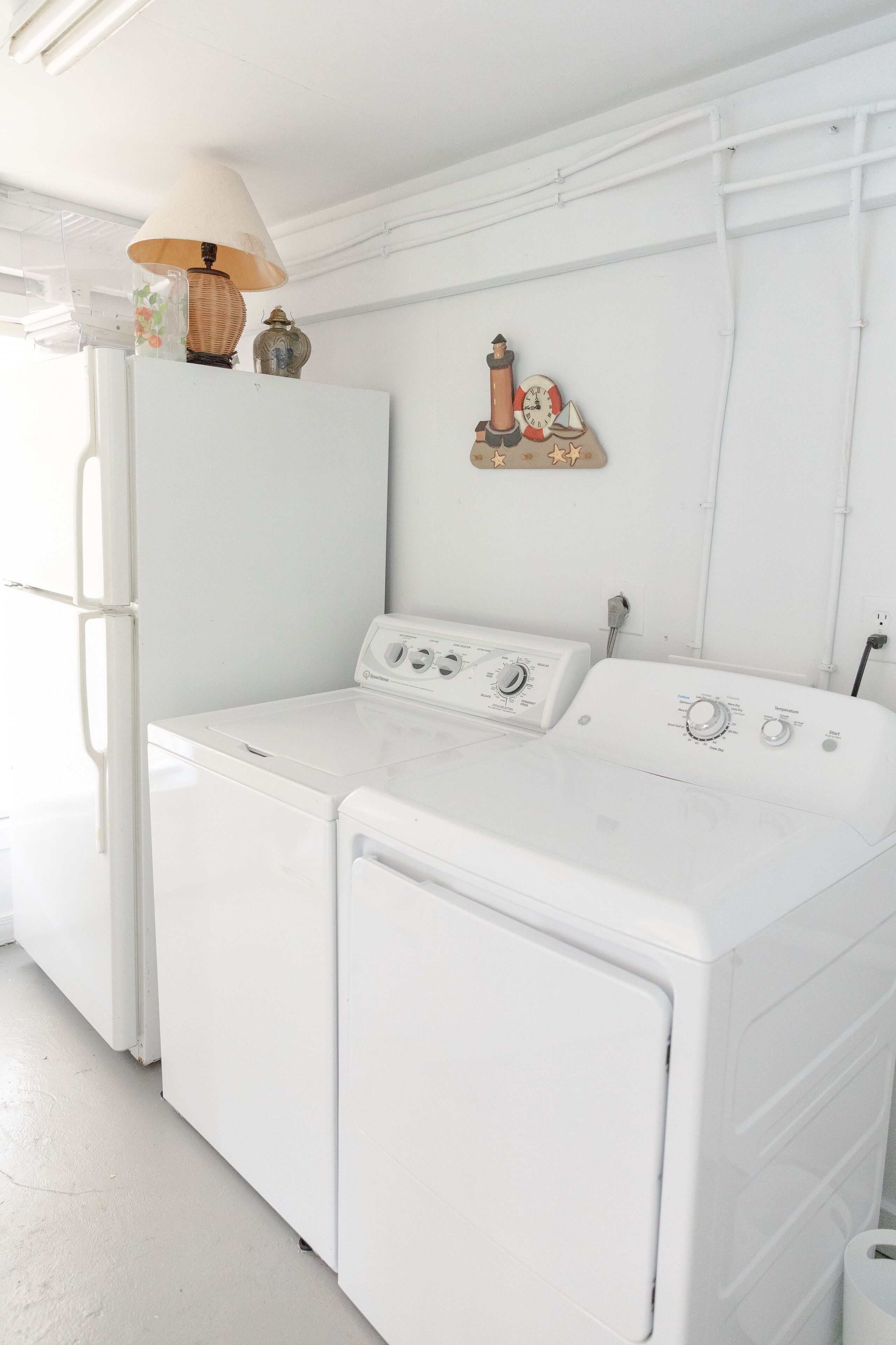 A laundry room with a front-loading washer and dryer, a small table with a lamp, and a decorative wall piece.