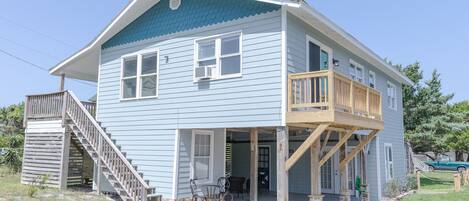 A two-story house with a wooden deck, a staircase, and a patio area with outdoor furniture.