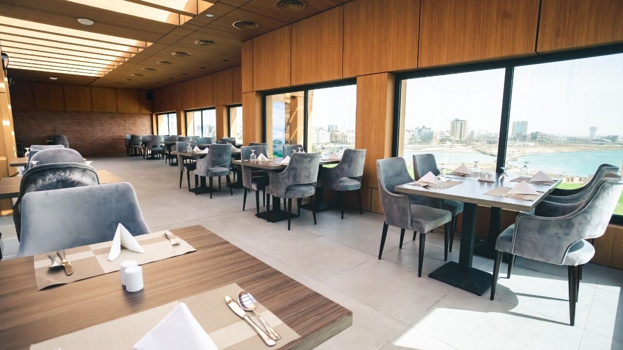 Un espace de restauration moderne, doté de tables et de chaises, et de grandes fenêtres offrant une vue sur la ville et le port.