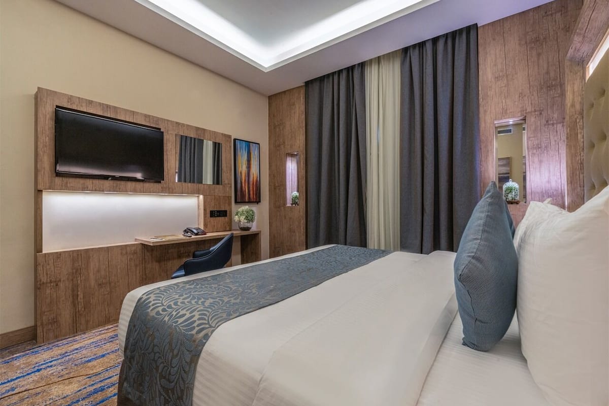 A hotel room with a large bed, a desk, a flat-screen TV, and a window with curtains.