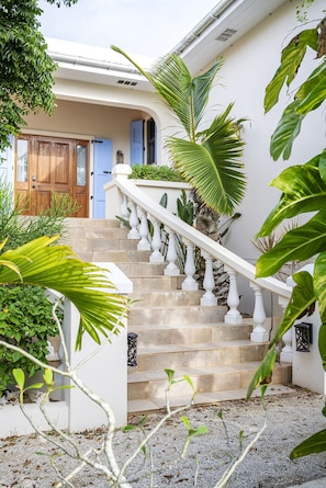 A staircase leading to a house with a white exterior, a blue door, and a wooden door.