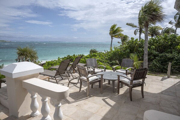 An outdoor seating area with a view of the ocean, surrounded by palm trees and greenery.