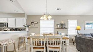 A modern kitchen with white cabinets, a dining table with chairs, a bar area, and a gray sofa in the living room. - TB 19E Eagle's Nest Beautiful three bedroom condo located in True Blue (PAWLEYS ISLAND)