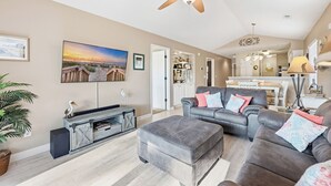 A spacious living room with a grey sectional sofa, a grey ottoman, and a large painting of a sunset. - TB 19E Eagle's Nest Beautiful three bedroom condo located in True Blue (PAWLEYS ISLAND)