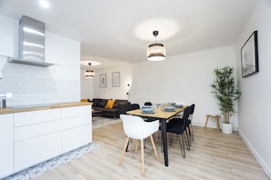 A modern kitchen with white cabinets, a wooden countertop, and a built-in stove. There is a dining area with a wooden table, black chairs, and a potted plant.