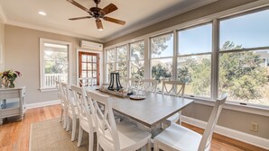 A dining area with a wooden table and white chairs, large windows with a view of trees, and a ceiling fan. - Come and Wind Down and Relax at Family Tides! (Georgetown)