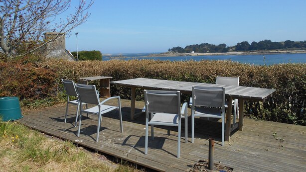 Eine Holzterrasse mit Tisch und Stühlen mit Blick auf ein Gewässer und entferntes Land.