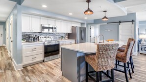 A modern kitchen with white cabinets, stainless steel appliances, and a central island with bar stools. - Gulf view, three bedroom, two bath condo in Mexico Beach. (Mexico Beach)