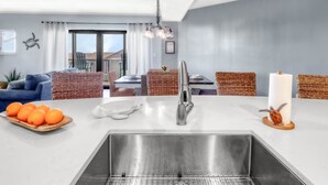 A modern kitchen with a stainless steel sink, a dining area with wicker furniture, and a view of the outdoors. - Gulf view, three bedroom, two bath condo in Mexico Beach. (Mexico Beach)