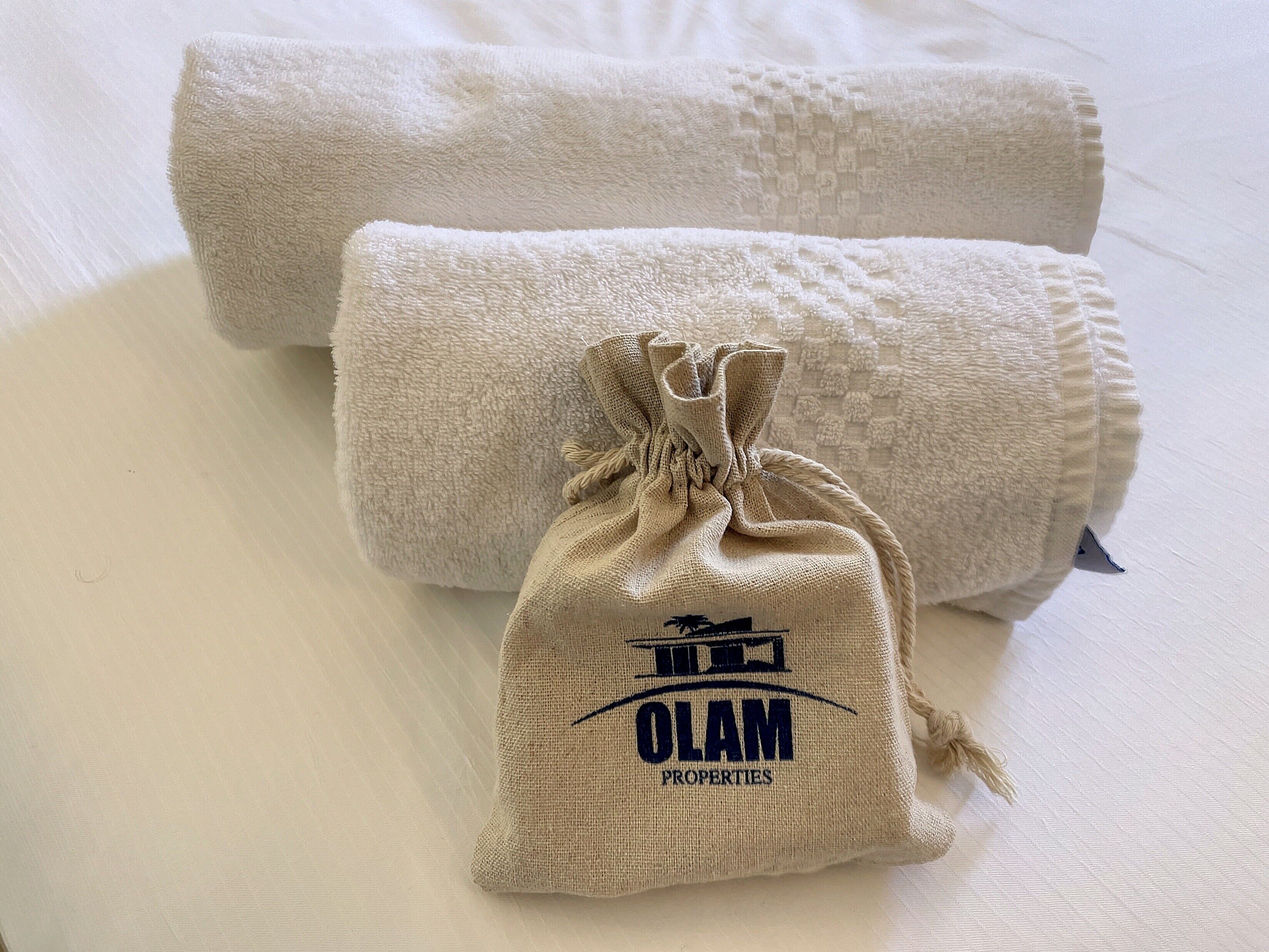 Two rolled towels and a small burlap sack with the text "OLAM PROPERTIES" on a white surface.