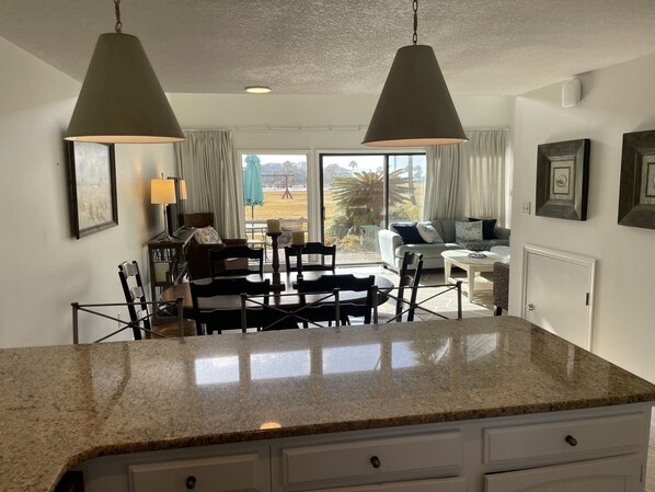 A kitchen with granite countertops, a dining area with chairs and a table, and a view of the outdoors through large windows. - Modern PCB Family Paradise near 30A,Ocean Views! (Panama City)