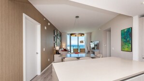 Interior moderno com área de jantar central, vista para o mar e uma grande pintura abstrata na parede.