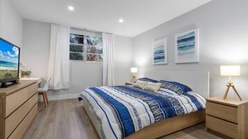 Quarto com cama, mesas de cabeceira, escrivaninha e televisão.