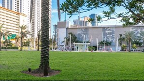 A grassy park area with a palm tree, a small kiosk, and a building with large windows in the background. - 2br Luxury Ocean Reserve With Park Views! 2 Bedroom Condo by RedAwning (Sunny Isles Beach)