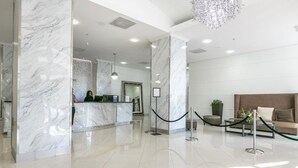A lobby with marble columns, a reception desk, a chandelier, and a seating area with a sofa and a plant. - 2br Luxury Ocean Reserve With Park Views! 2 Bedroom Condo by RedAwning (Sunny Isles Beach)