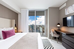 A modern hotel room with a large bed, a desk, a chair, a TV, and a balcony with a city view. - Hyde Beach House Luxury -resort 3 Bedroom Condo by RedAwning (Hollywood)
