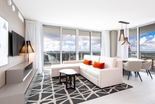 A modern living room with a white sofa, a small round table, and a large window offering a city view. - Hyde Beach House Luxury -resort 3 Bedroom Condo by RedAwning (Hollywood)