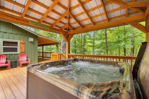 A wooden deck with a hot tub, two red Adirondack chairs, and a covered area with a sign. - Beside Still Water 2 - 2 Bedrooms, 2 Baths, Sleeps 6 Home by RedAwning (Cosby)